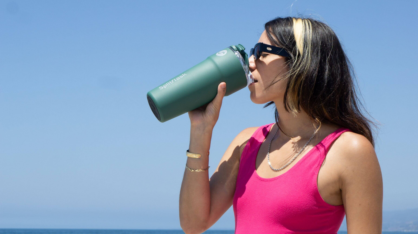 Lady drinking form a green splitflask with the ocean in the distance